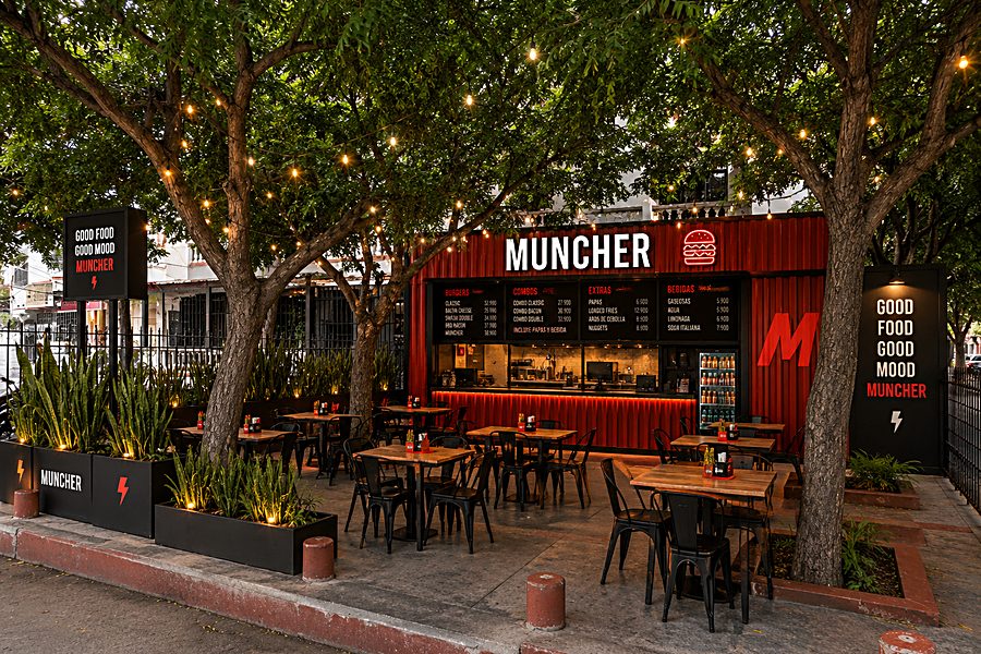 Render de la terraza de Muncher Villa Carolina: cocina en contenedor rojo, mesas bajo los árboles y luces colgantes